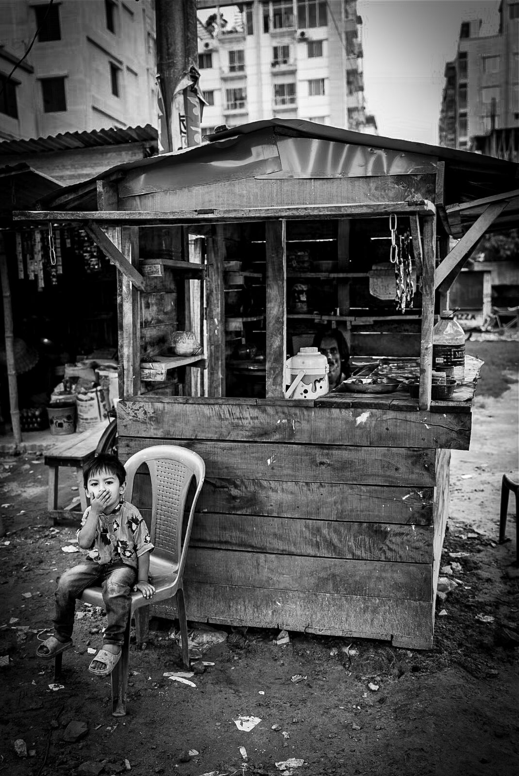 Child sitting on a chair beside a wooden roadside stall