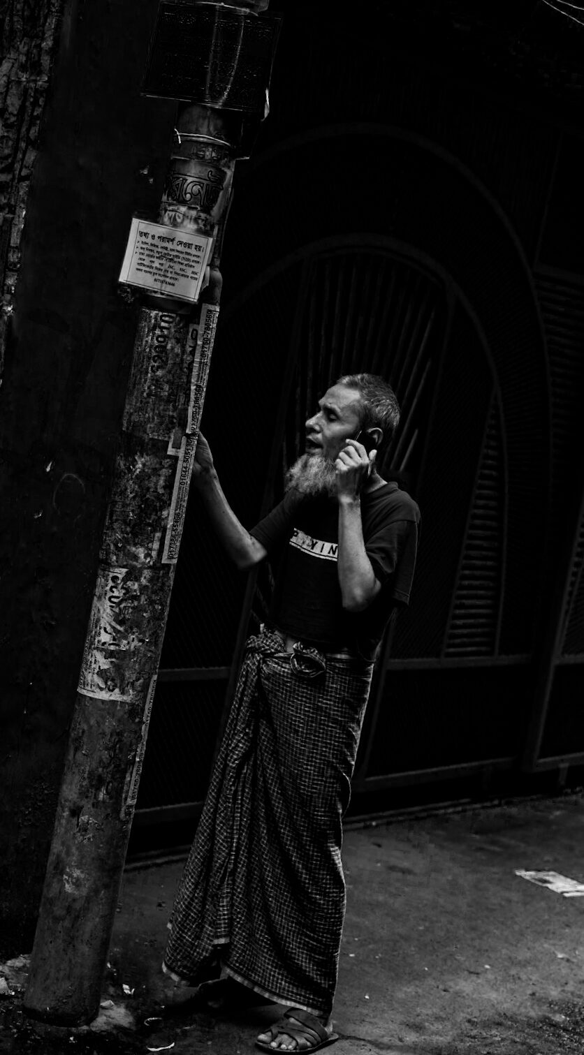Man on a phone call leaning against a pole