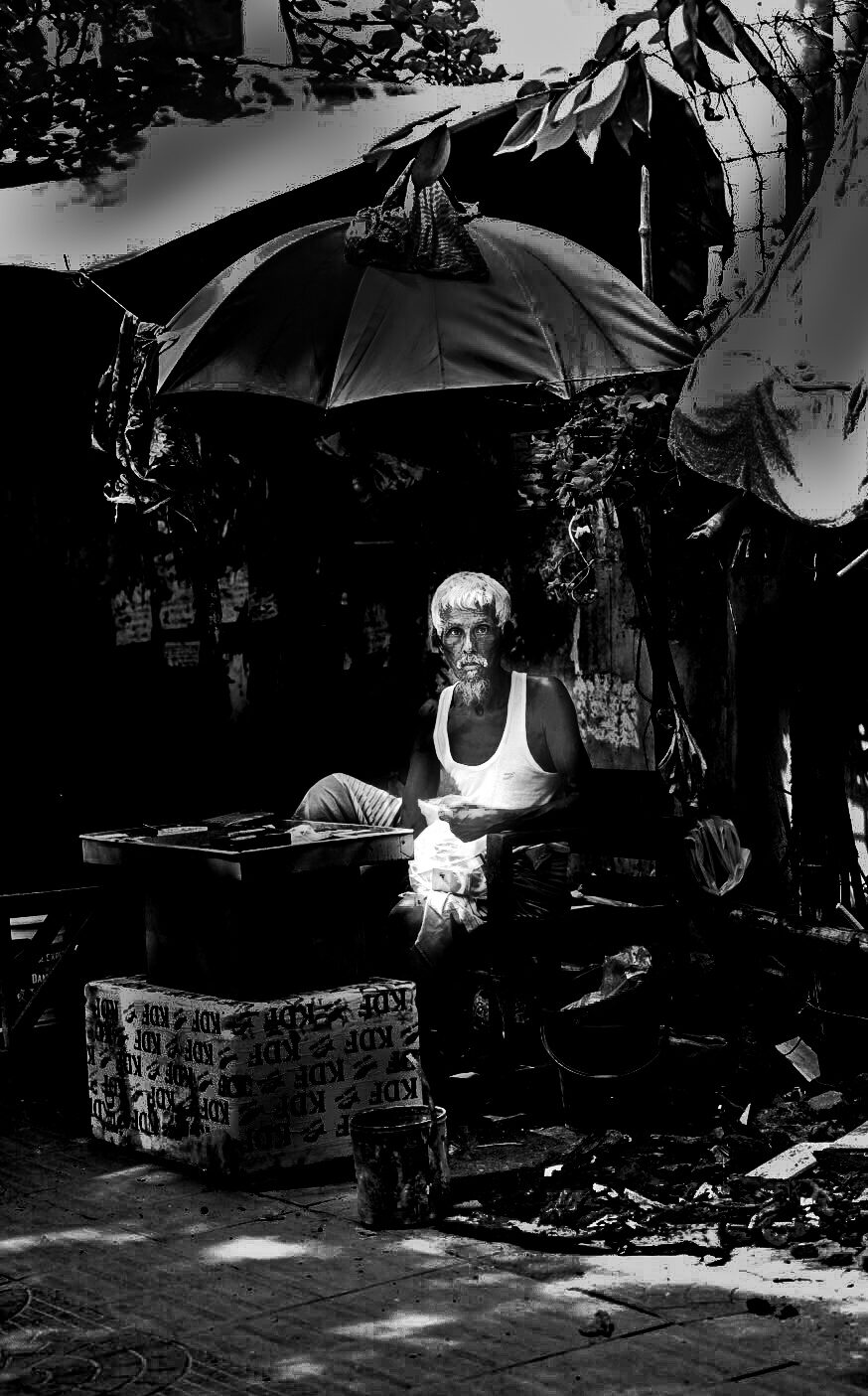 Elderly man sitting under an umbrella at his stall