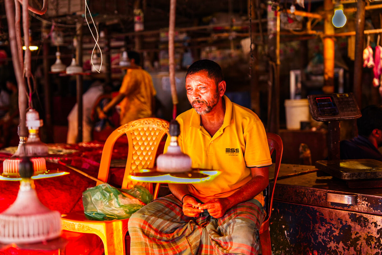 Man in a yellow shirt sitting in a market lit by warm light