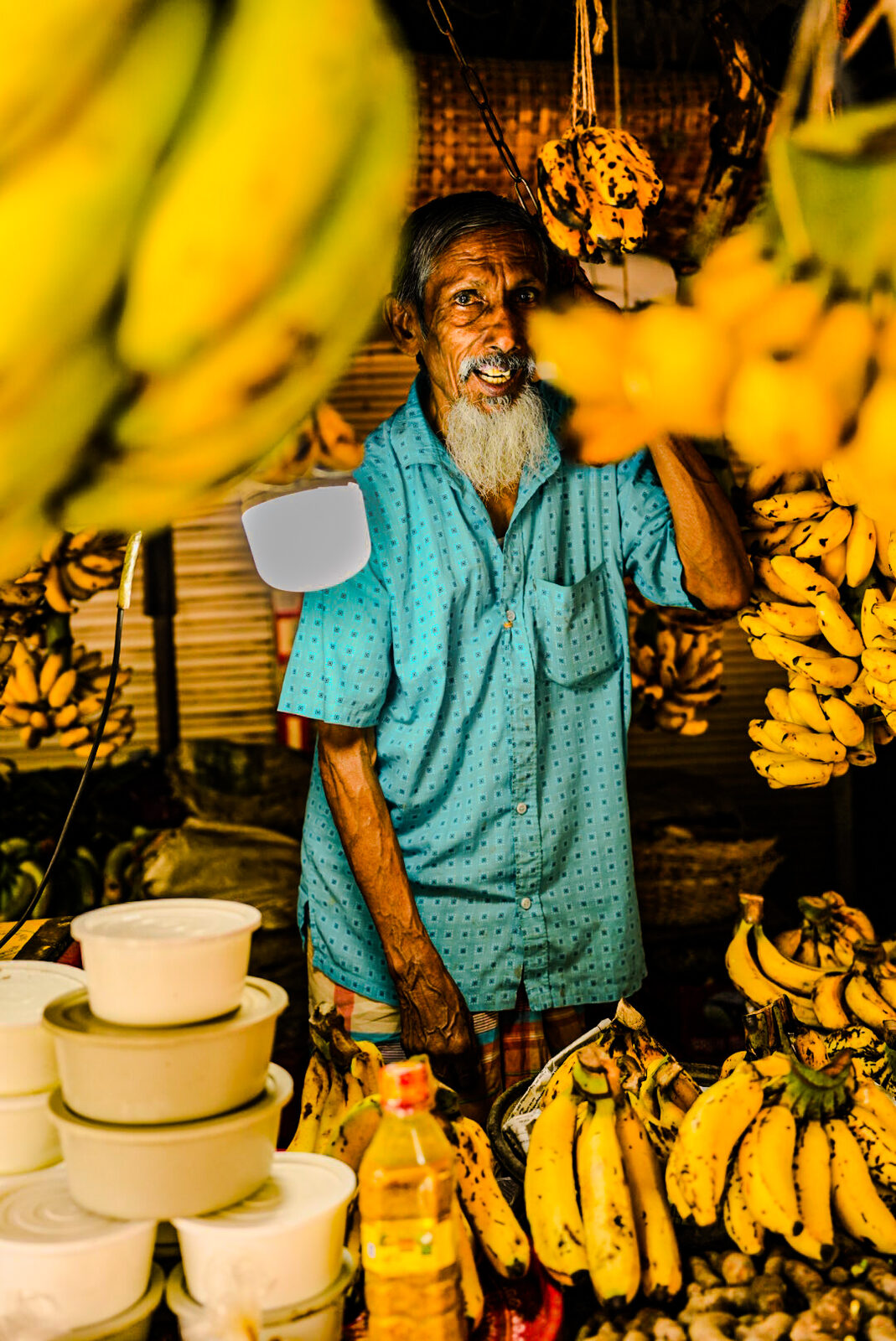Banana vendor smiling among hanging bananas
