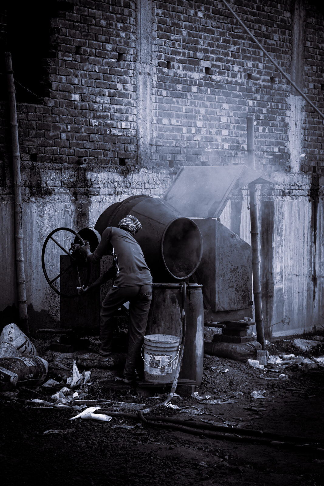 Worker operating a cement mixer against a brick wall